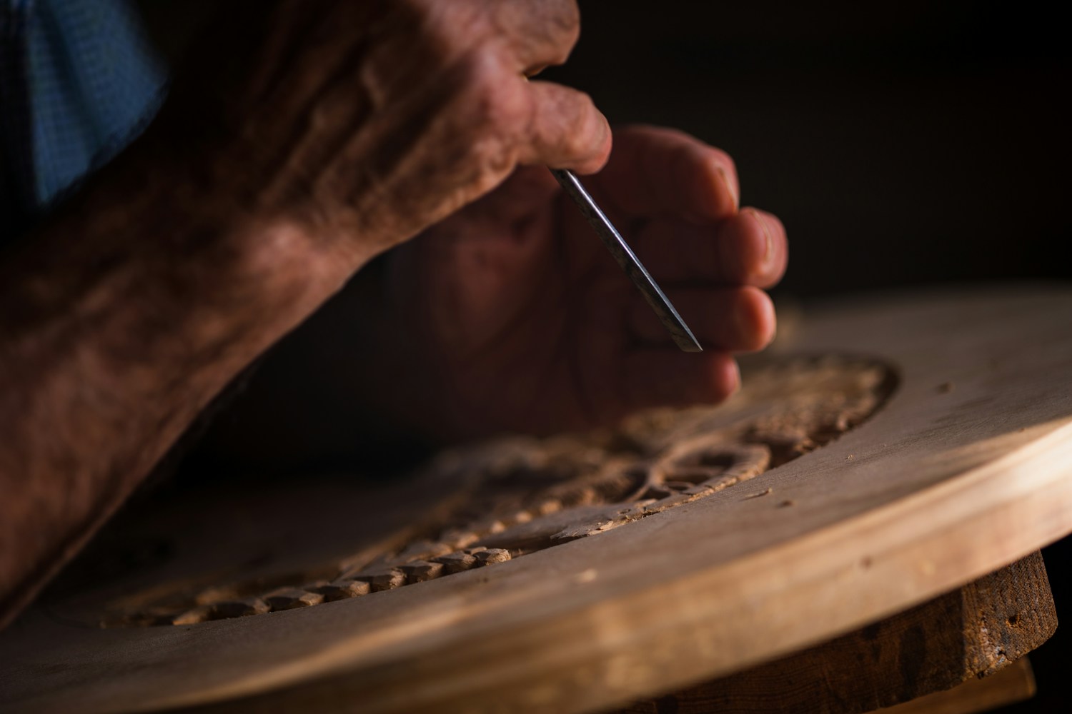 Close view of a craftsperson carving a decorative pattern into wood with a small hand tool.