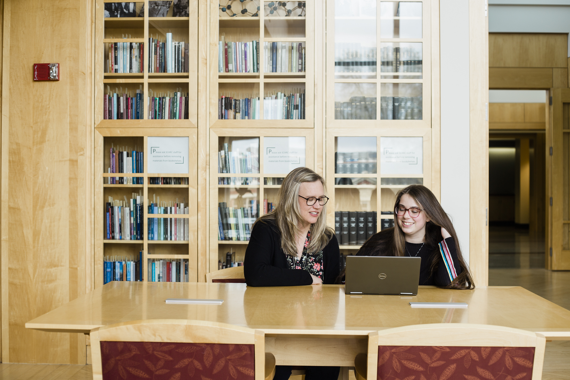 A librarian and a student review Wikipedia together at a table in a sunlit library.